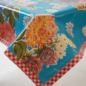 May include: A turquoise floral tablecloth with a red and white checkered border. The tablecloth features large, colorful flowers in shades of orange, pink, and white. The design is reminiscent of vintage styles.