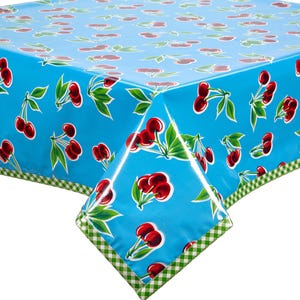 May include: A blue tablecloth with a repeating pattern of red cherries and green leaves. The edges are trimmed with a green and white checkered border. The tablecloth is made of a shiny, waterproof material.
