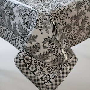 May include: Black and white tablecloth with a floral pattern and a black and white checkered border. The tablecloth is made of vinyl and has a glossy finish.