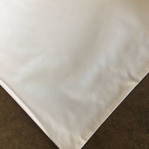 May include: A white vinyl tablecloth with a smooth, glossy finish. The tablecloth has a stitched edge.