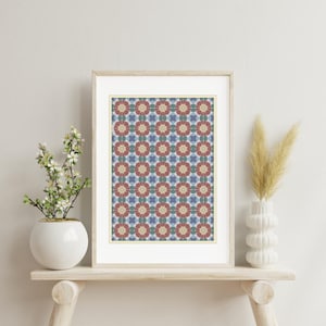 Può includere: Una stampa incorniciata con un motivo floreale ripetuto nei colori rosso, blu e crema. L'opera d'arte è esposta su una mensola di legno chiaro, con un vaso bianco con fiori a sinistra e un vaso decorativo con erba secca a destra.