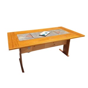 May include: A rectangular wooden dining table featuring a light brown wood grain finish and a central inlay of gray stone tiles arranged in a geometric pattern. A small white rectangular tile with blue accents rests on the table surface.