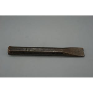 May include: A dark gray metal cold chisel with a hexagonal shaft and a flat, beveled cutting edge. The side of the tool features the stamped text "DRR ALLOY" in capital letters. The metal surface shows signs of wear, oxidation, and texture.