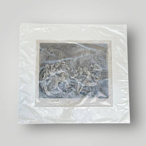 May include: A black and white engraving depicting a group of people gathered around a table. The scene is set in a dimly lit room with a ghost-like figure in the background. The engraving is framed in a white mat and a clear plastic sleeve.