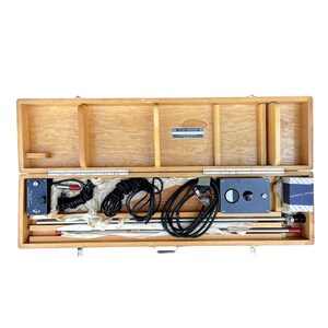 May include: A wooden carrying case with a black and silver measuring device, a black cord, and a red and black cord. The case has a label that reads "AKAI ELECTRIC CO., LTD."