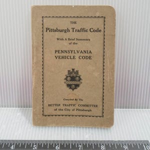 May include: A vintage booklet titled "The Pittsburgh Traffic Code" with text detailing the Pennsylvania Vehicle Code. The cover is a light brown color with black text and a decorative emblem. Compiled by the Better Traffic Committee.