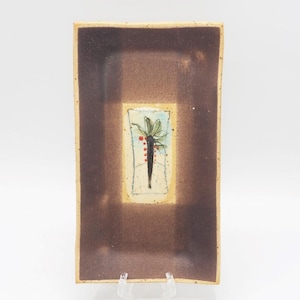 May include: Rectangular ceramic dish with a brown border and a central design. The design features a stylized plant with green leaves and red berries on a light blue background. The dish is supported by a clear plastic stand.