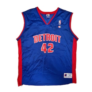 May include: Blue Detroit basketball jersey with red accents. The jersey features the word "DETROIT" in white block letters across the chest, with the number "42" below it in red. The jersey has a V-neck and the Champion logo.