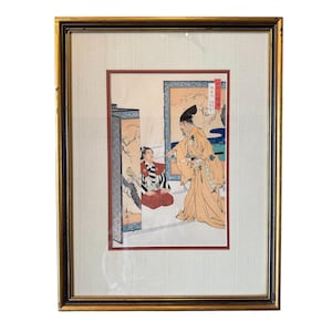 Puede incluir: Grabado japonés enmarcado que representa una escena con dos figuras vestidas con trajes tradicionales. El grabado muestra a un hombre con una túnica amarilla gesticulando hacia una figura sentada. La obra de arte está enmarcada en un marco dorado.