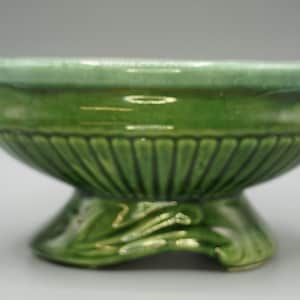 May include: A green ceramic pedestal bowl with a fluted body and a leaf-like base. The rim is a lighter shade of green. The bowl is approximately 5 inches in diameter and 4 inches tall.