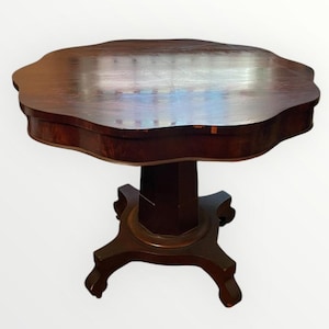 May include: A dark brown antique table with a unique, scalloped edge. The table has a pedestal base with four curved legs. The tabletop appears to be made of wood and has a polished finish. The table is a classic piece of furniture.