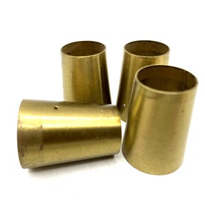 May include: Four brass cone-shaped objects with a slightly tarnished finish. The objects are hollow and have a cylindrical top opening. One object has a small hole near the top. The objects are arranged on a white surface.
