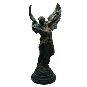 Op de afbeelding: Bronzen sculptuur met twee omhelzende figuren, een met grote, gedetailleerde vleugels. De figuren zijn naakt, met gedrapeerde stof rond het onderlichaam. De sculptuur is gemonteerd op een ronde, donkere basis.