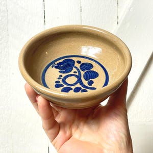 Puede incluir: Un pequeño cuenco de cerámica marrón con un diseño floral azul. El cuenco está pintado a mano con un patrón floral azul.