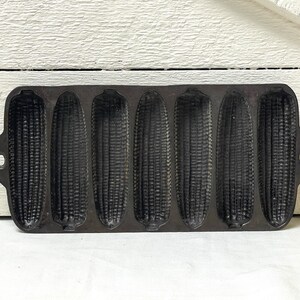 May include: A black cast iron cornbread pan with six individual moulds shaped like corn cobs.