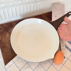 May include: White enamel cast iron skillet with a black handle on a wooden chopping board. A brown egg is sitting next to the skillet.