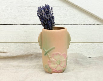 May include: A pale pink ceramic vase with a floral design and two sculpted faces on the sides. The vase is filled with dried lavender.