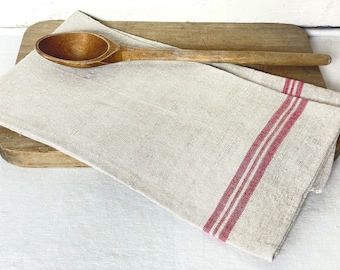 May include: A white linen tea towel with red stripes, folded over a wooden cutting board with a wooden spoon on top.
