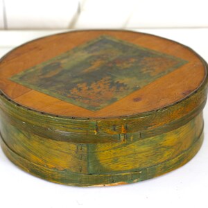 May include: A round wooden box with a green painted exterior and a wood lid with a faded image of a landscape scene. The box is approximately 8 inches in diameter.