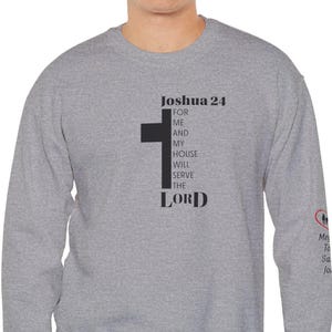 Könnte beinhalten: Ein meliertes graues Sweatshirt mit dem Text "Joshua 24" und einer schwarzen Kreuzgrafik. Der Text "For me and my house will serve the Lord" ist vertikal gedruckt. Das Sweatshirt hat lange Ärmel.