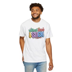 A man with curly hair smiles while wearing a white t-shirt with "Without Jesus I Suck" in colorful, graffiti-style text.