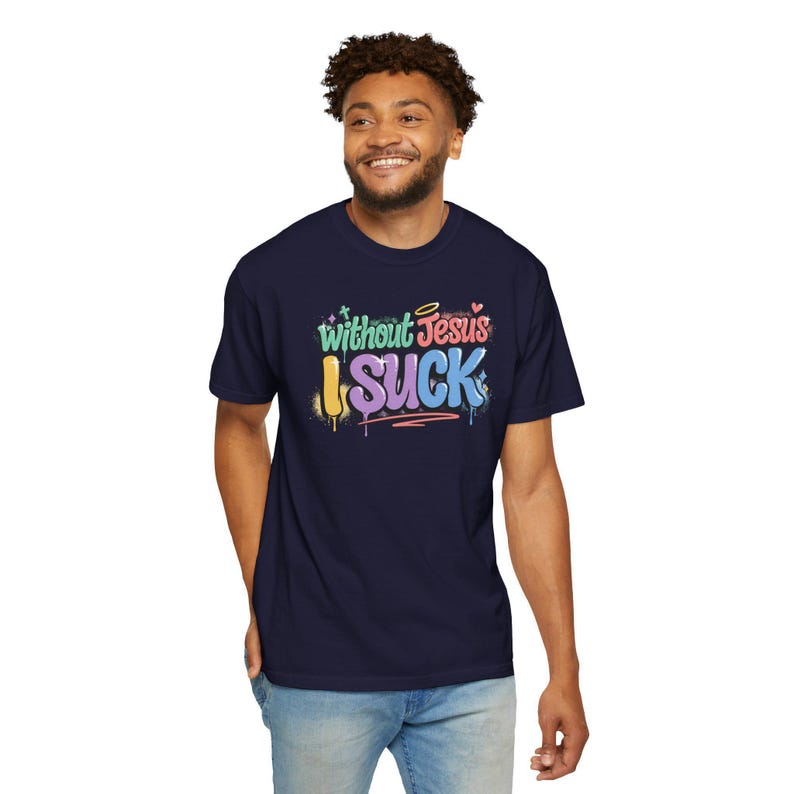 A man with curly hair smiles while wearing a navy t-shirt with "Without Jesus I Suck" in colorful, graffiti-style text.