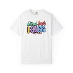 A white t-shirt with the colorful graffiti-style text "Without Jesus I Suck" is laid flat against a white background.