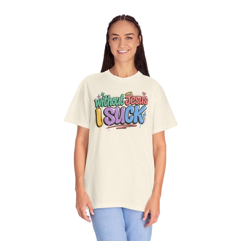A woman with braided hair smiles while wearing an off-white t-shirt with "Without Jesus I Suck" in colorful, graffiti-style text.