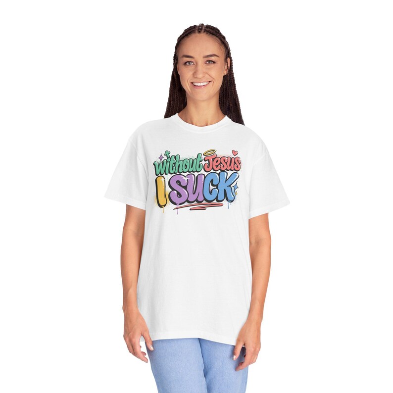 A woman with braided hair smiles while wearing a white t-shirt with "Without Jesus I Suck" in colorful, graffiti-style text.