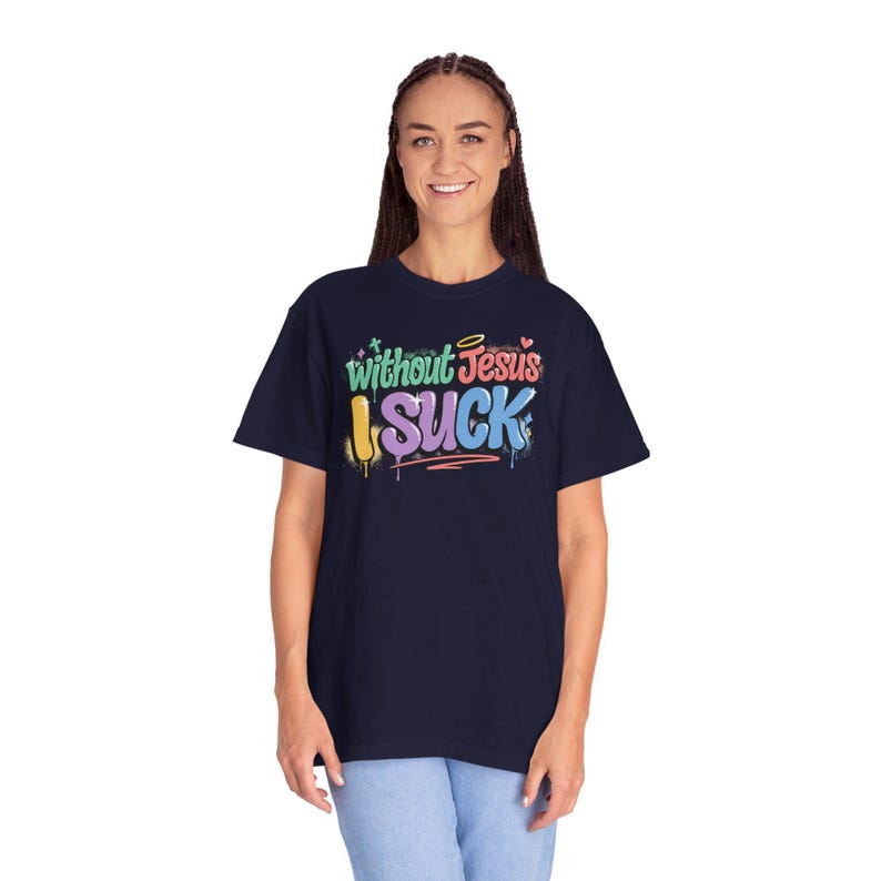A woman with braided hair smiles while wearing a navy t-shirt with "Without Jesus I Suck" in colorful, graffiti-style text.