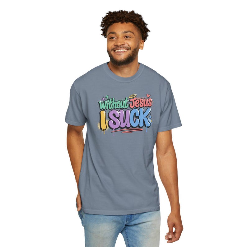 A man with curly hair smiles while wearing a light blue t-shirt with "Without Jesus I Suck" in colorful, graffiti-style text.