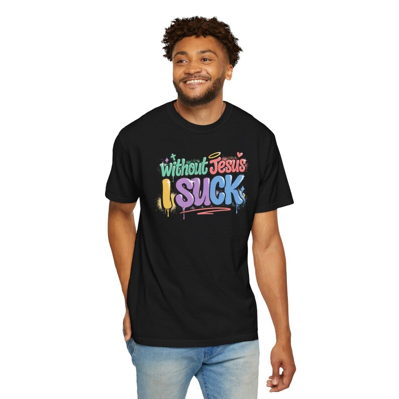 A man with curly hair smiles while wearing a black t-shirt with "Without Jesus I Suck" in colorful, graffiti-style text.