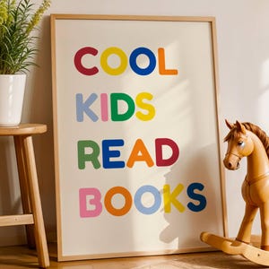 Peut inclure: Une affiche encadrée avec les mots "COOL KIDS READ BOOKS" en lettres majuscules colorées. Un cheval à bascule en bois et une plante en pot sont à proximité. L'affiche a un fond beige clair et un cadre en bois.