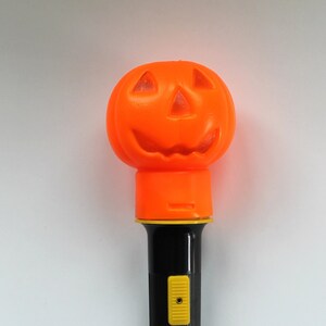 May include: Orange plastic pumpkin shaped flashlight with a black handle and a yellow button. The flashlight has the words "Flash-N-Flash" printed on the handle.