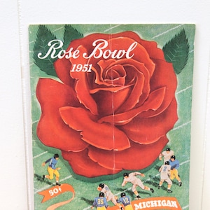 May include: A vintage Rose Bowl program from 1951 featuring a large red rose with green leaves. The program cover also shows a football game with players from the University of California and the University of Michigan. The text on the cover reads "Rose Bowl 1951" and "50¢".