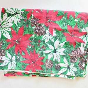 May include: A green, white, and red Christmas tablecloth with a poinsettia pattern. The tablecloth is folded in half and has a white background with red poinsettias and green pine branches.