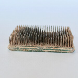 May include: A vintage floral arranging tool with a wooden base and metal pins. The base is green and the pins are rusty.