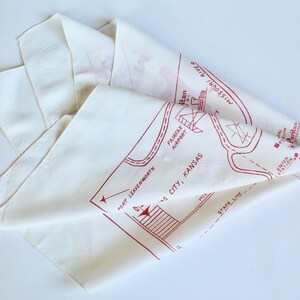 May include: White cotton bandana with a red map of Kansas City, Kansas. The map includes the Missouri River, Fairfax Airport, and the Union Station. The text "Fort Leavenworth" is also included on the map.