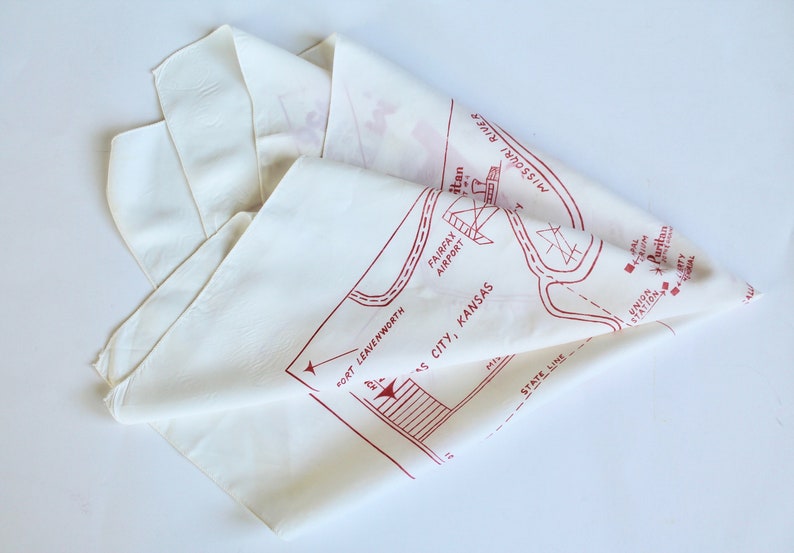 May include: White cotton bandana with a red map of Kansas City, Kansas. The map includes the Missouri River, Fairfax Airport, and the Union Station. The text "Fort Leavenworth" is also included on the map.
