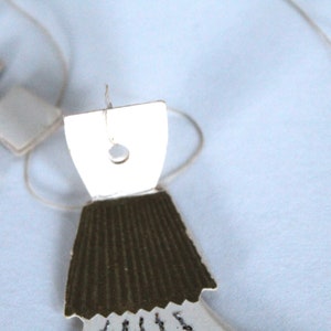 May include: A white paper doll with a brown paper skirt and a hole in the top for hanging. The doll is hanging from a string.