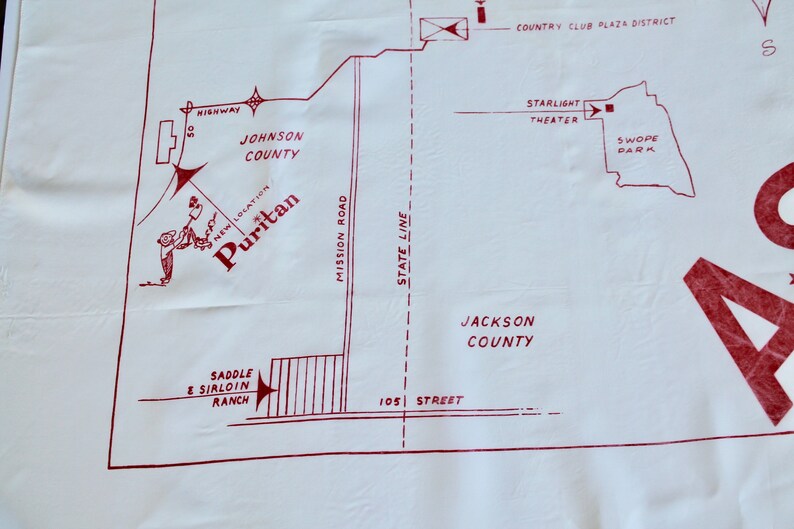 May include: A red and white map of a city with the words "Puritan", "Johnson County", "Jackson County", "Mission Road", "State Line", "105 Street", "Saddle & Sirloin Ranch", "Country Club Plaza District", "Starlight Theater", and "Swope Park".