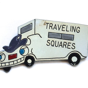 May include: White enamel pin of a cartoon van with a smiling face, a blue hat, and the words "TRAVELING SQUARES" on the side.