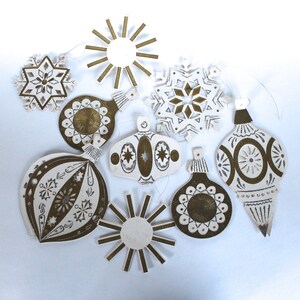 May include: A set of nine white paper Christmas ornaments with gold glitter accents. The ornaments feature various designs, including snowflakes, stars, and geometric patterns.
