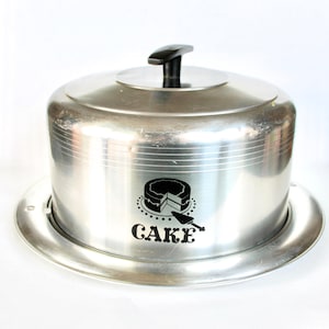 May include: Silver cake dome with a black handle and a black graphic of a cake slice with the word "CAKE" underneath.
