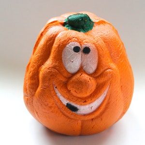 May include: Orange foam pumpkin with a green stem and a painted face. The pumpkin has a wide smile with a black tooth and large, round eyes.