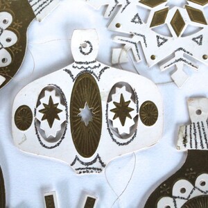 May include: A set of vintage paper Christmas ornaments with gold and silver glitter. The ornaments are shaped like stars, snowflakes, and bells.
