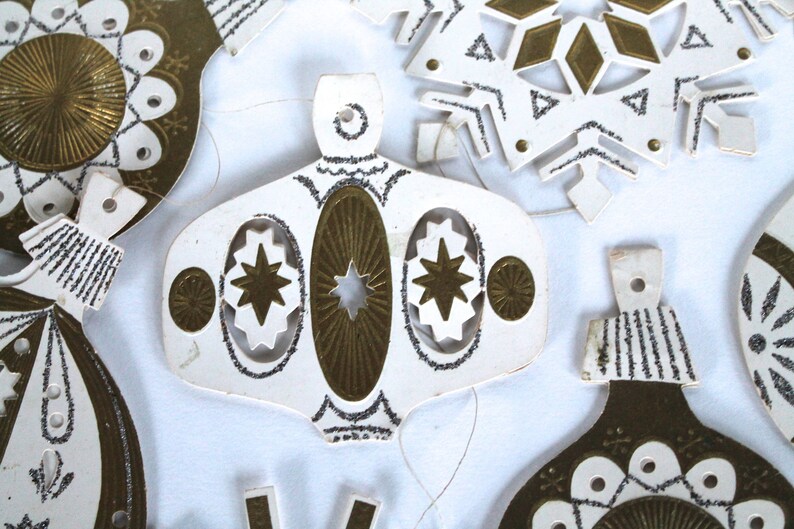 May include: A set of vintage paper Christmas ornaments with gold and silver glitter. The ornaments are shaped like stars, snowflakes, and bells.