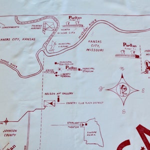 May include: A vintage map of Kansas City, Missouri, with red text and lines on a white background. The map shows the location of various landmarks, including the Municipal Auditorium, Liberty Memorial, Municipal Stadium, Nelson Art Gallery, Country Club Plaza District, Starlight Theater, Swope Park, and the origin of the Santa Fe Trail. The map also includes the text "Puritan Plant No. 1" and "Puritan Plant No. 2".