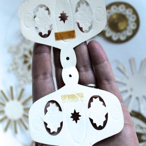 May include: White paper ornament with a star and cut-out designs. The ornament is in two pieces that are connected by a small hole in the center.