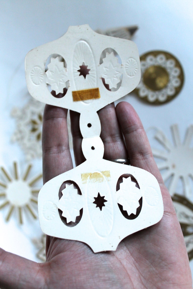 May include: White paper ornament with a star and cut-out designs. The ornament is in two pieces that are connected by a small hole in the center.